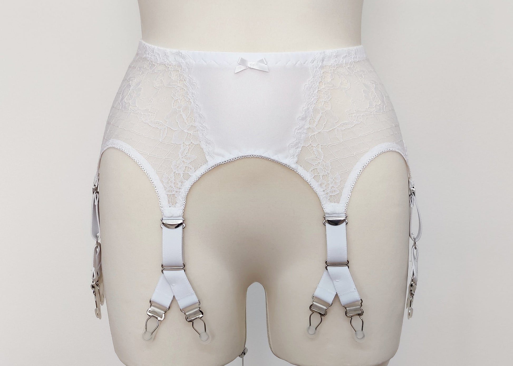 A white lace Rita garter belt with 6 Y-straps and a bow detail, displayed on a mannequin.
