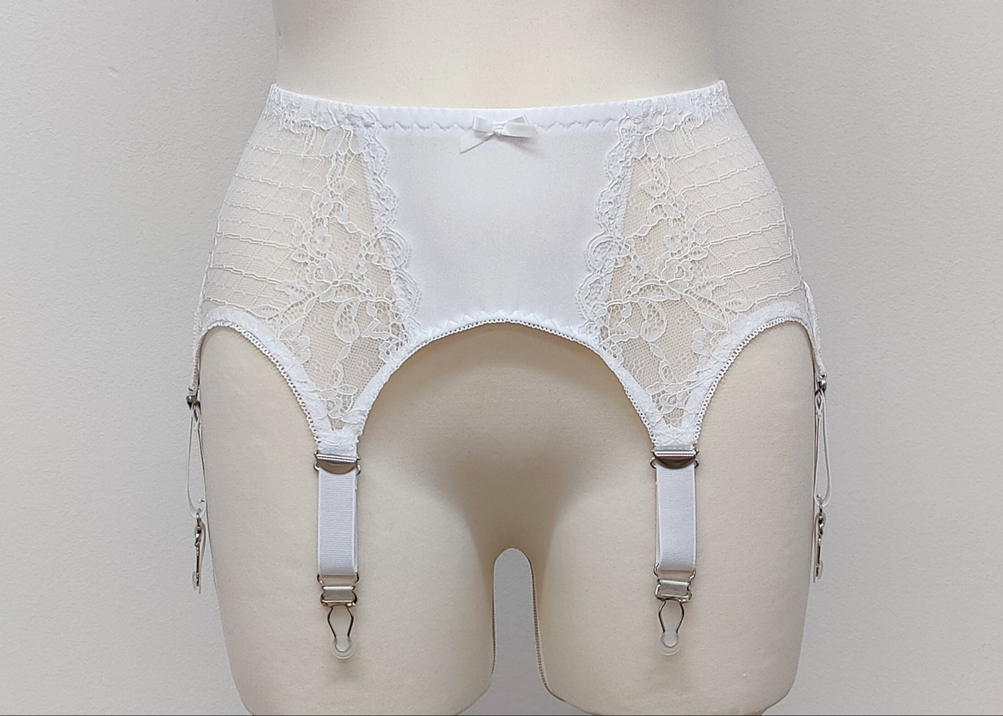 A white lace Mona garter belt with 6 adjustable straps and hook and eye closure, displayed on a mannequin.