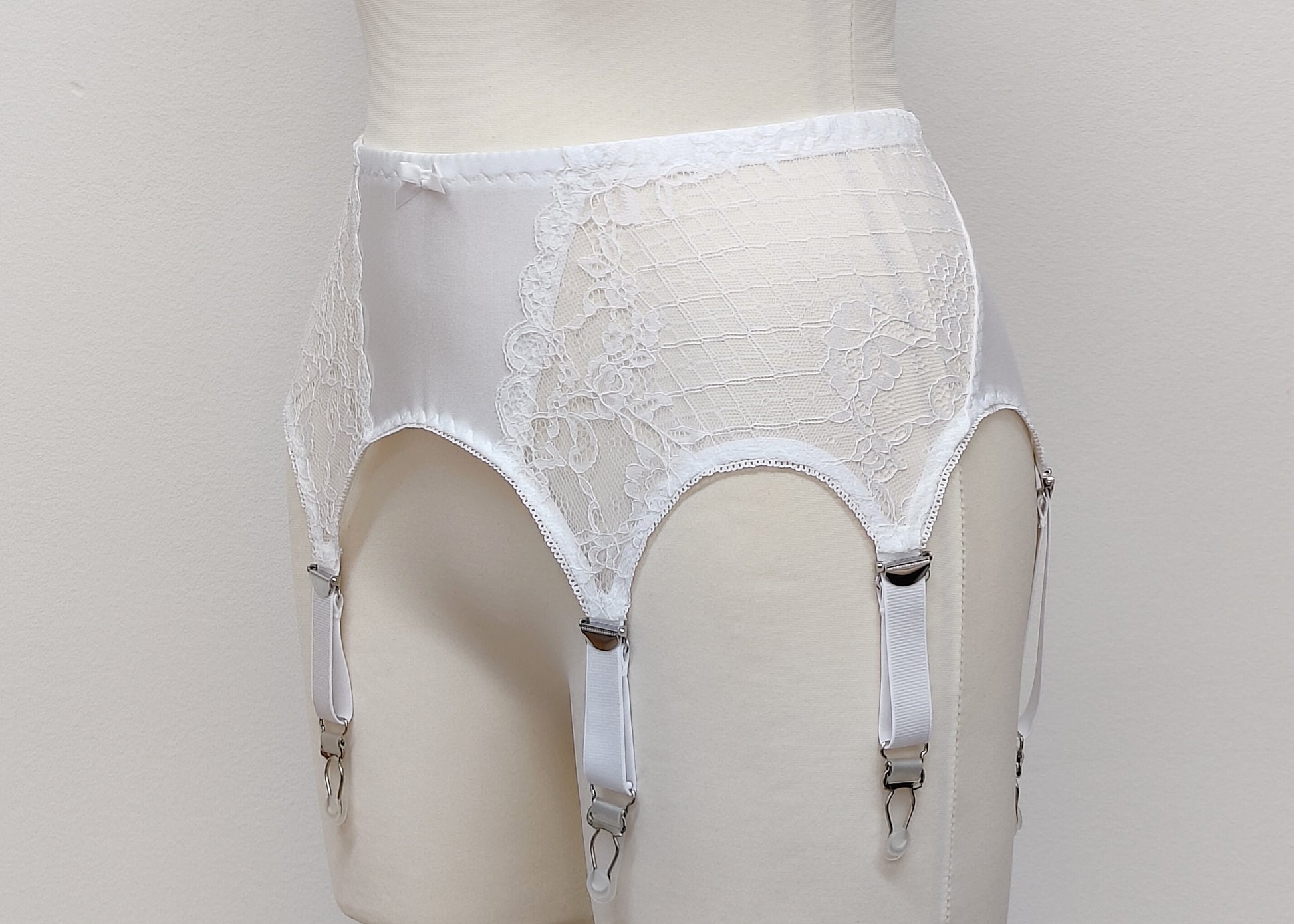 A white lace Mona garter belt with 6 adjustable straps and hook and eye closure, displayed on a mannequin, side view