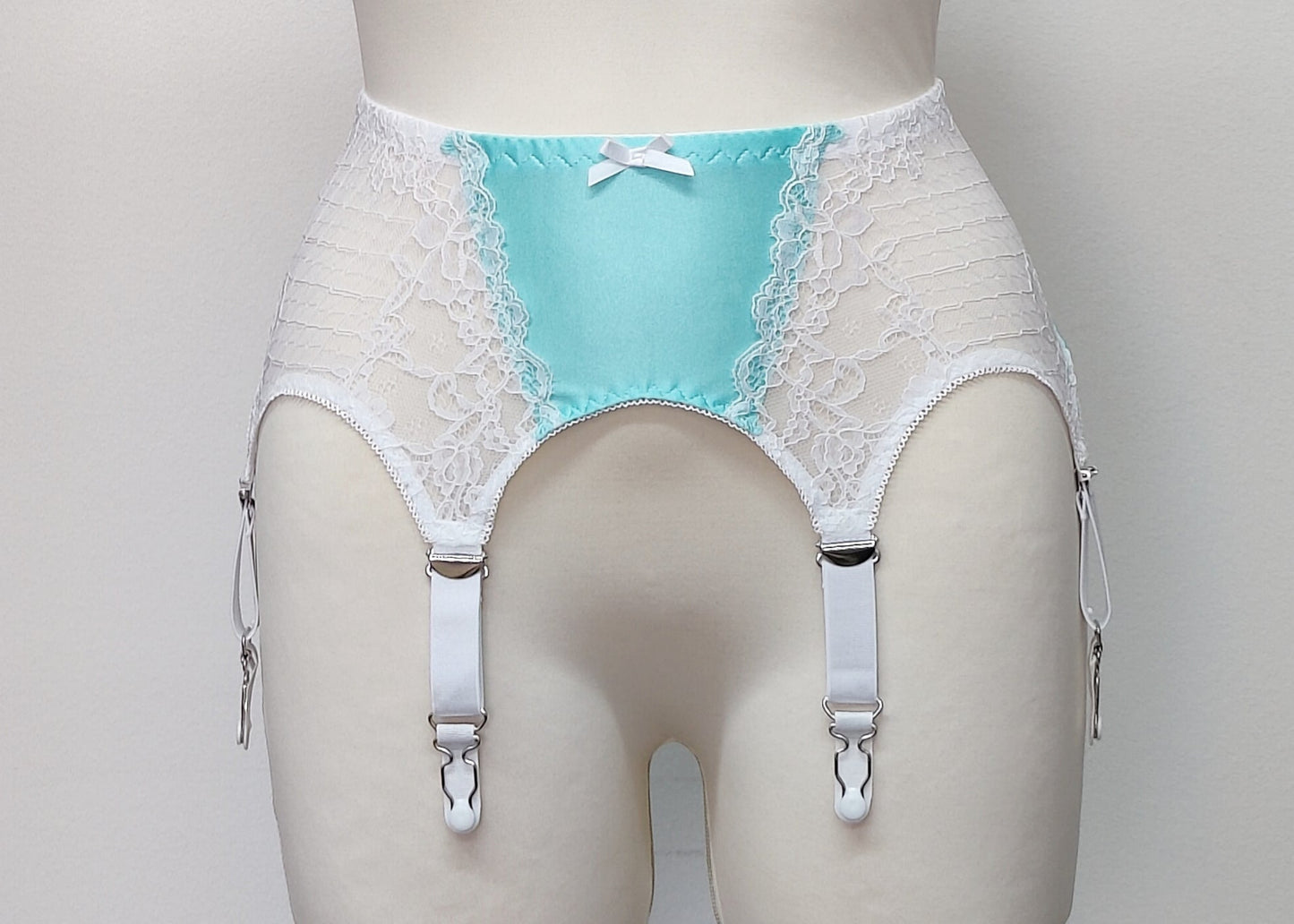 A white lace and Aqua blue Lycra, Mona garter belt with 6 adjustable straps and hook and eye closure, displayed on a mannequin.