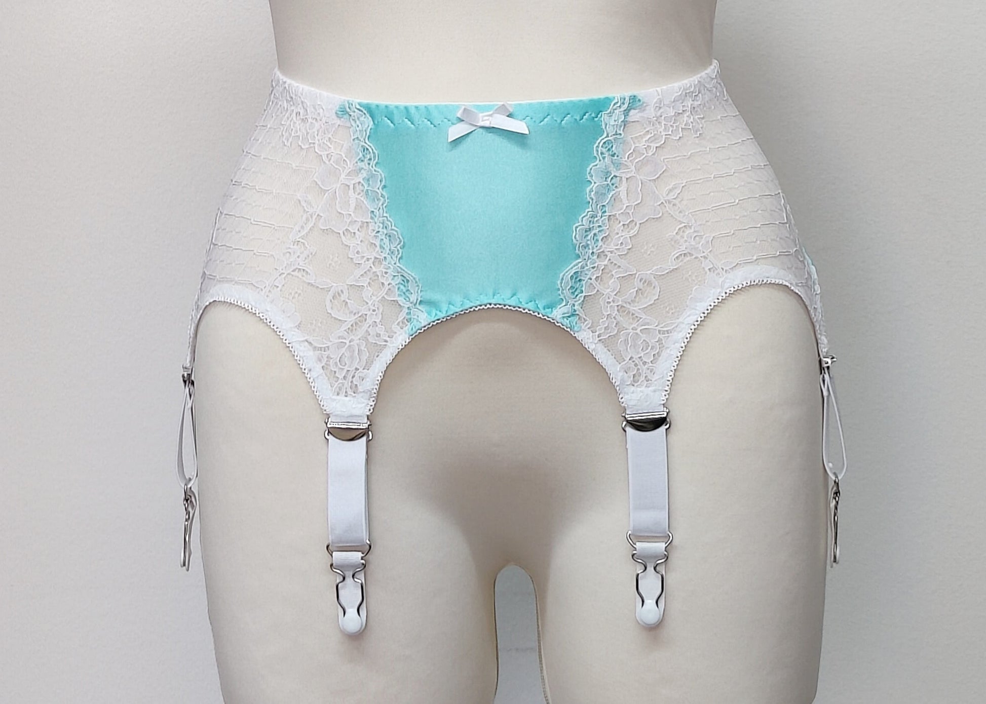A white lace and Aqua blue Lycra, Mona garter belt with 6 adjustable straps and hook and eye closure, displayed on a mannequin.