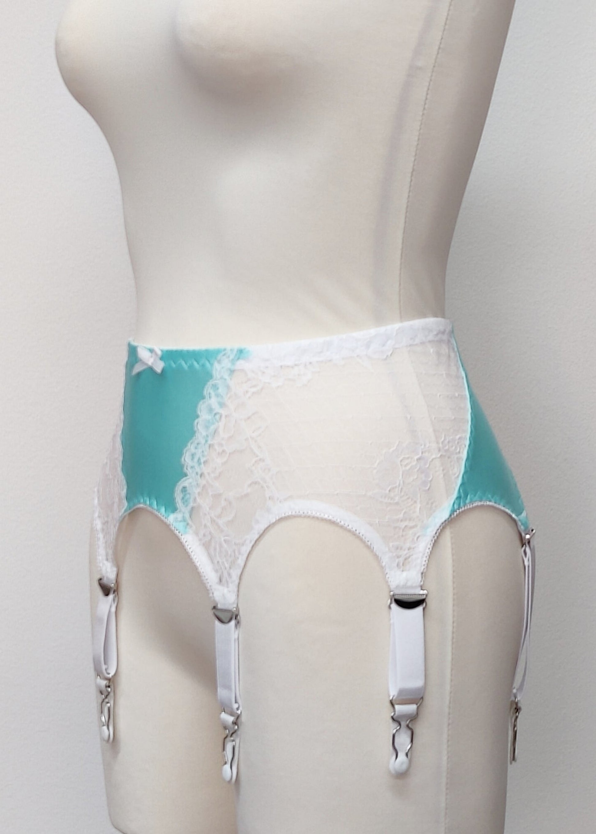 A white lace and Aqua blue Lycra, Mona garter belt with 6 adjustable straps and hook and eye closure, displayed on a mannequin, side view