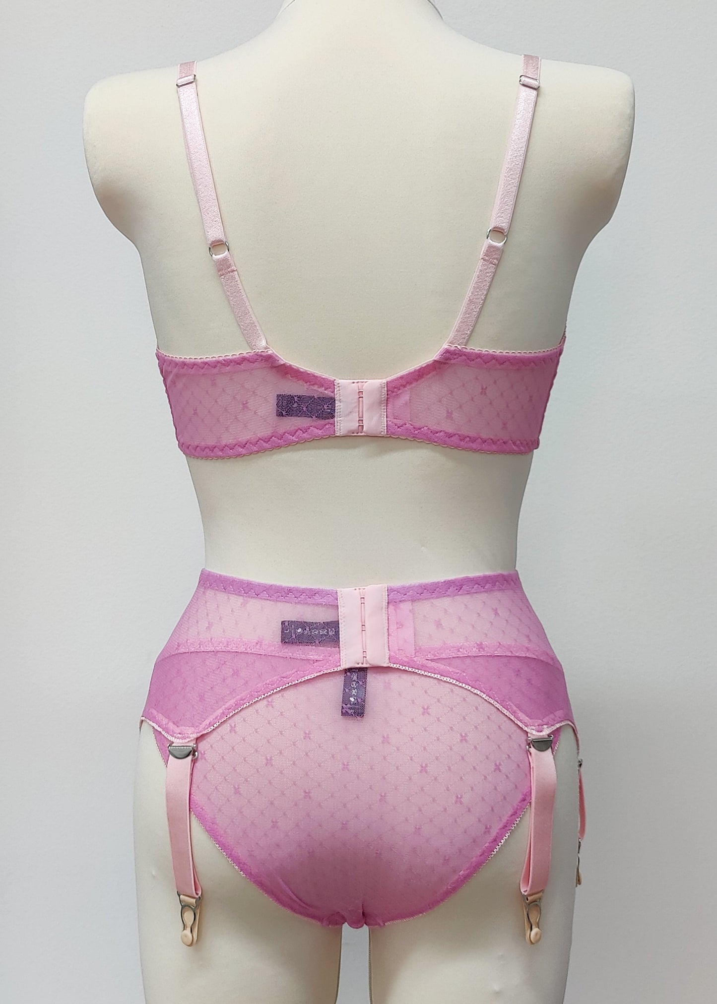 A pink sheer LULA garter belt with adjustable straps displayed on a mannequin. The belt has a transparent mesh design with pink accents and metal hardware. back view