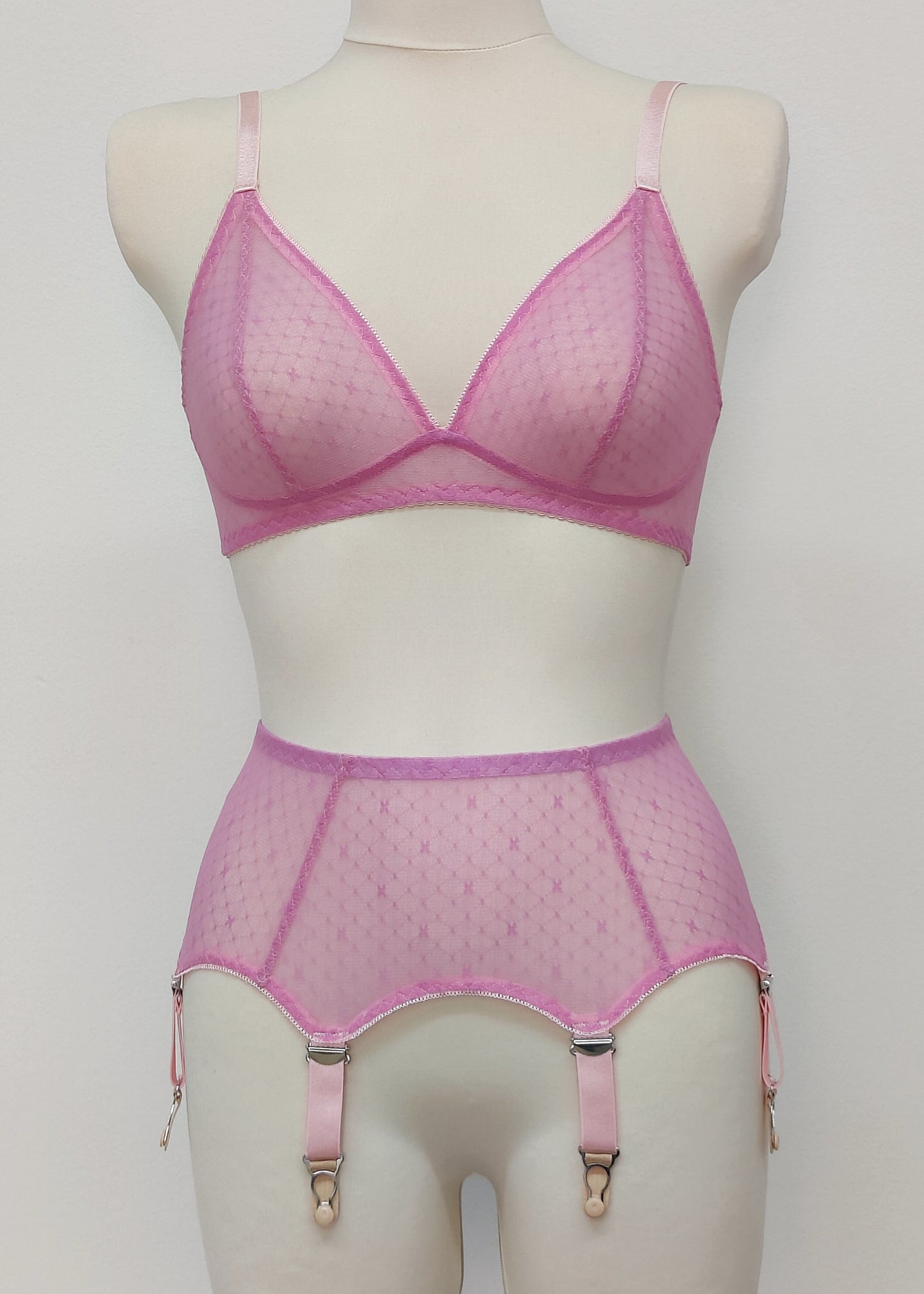Pink sheer LULA garter belt with 6 adjustable straps displayed on a mannequin. The belt has a transparent mesh design with pink accents and metal hardware.