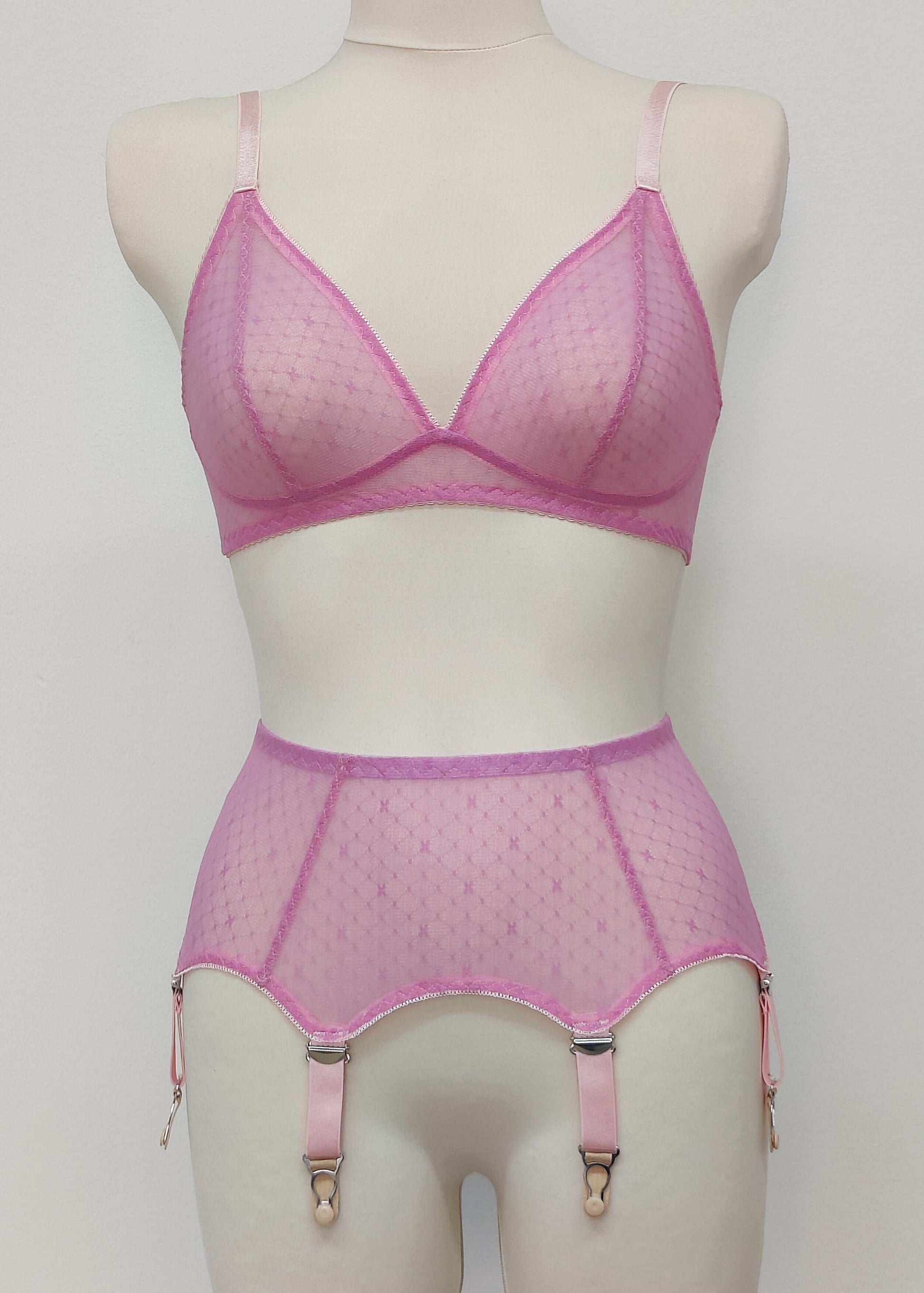 Pink sheer LULA garter belt with 6 adjustable straps displayed on a mannequin. The belt has a transparent mesh design with pink accents and metal hardware.