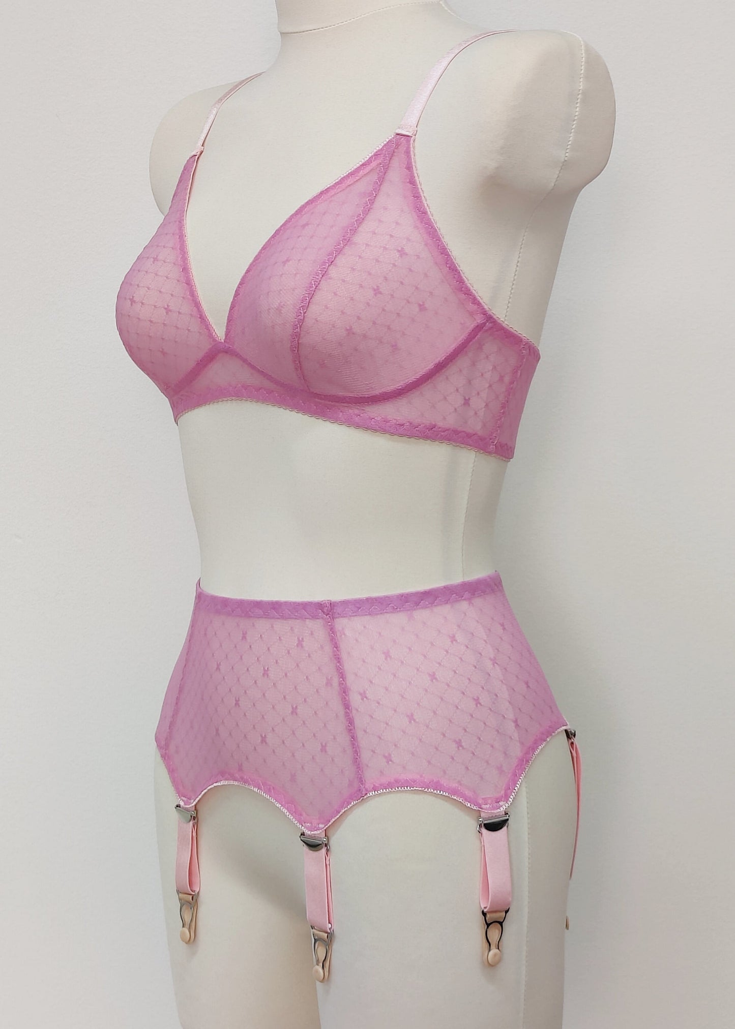 Pink sheer LULA garter belt with 6 adjustable straps displayed on a mannequin. The belt has a transparent mesh design with pink accents and metal hardware. side view