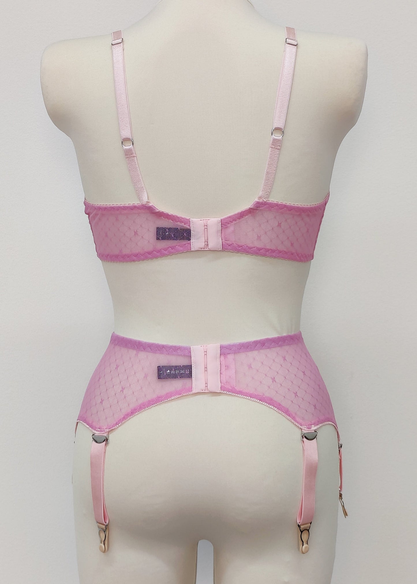 Pink sheer LULA garter belt with 6 adjustable straps displayed on a mannequin. The belt has a transparent mesh design with pink accents and metal hardware. back view