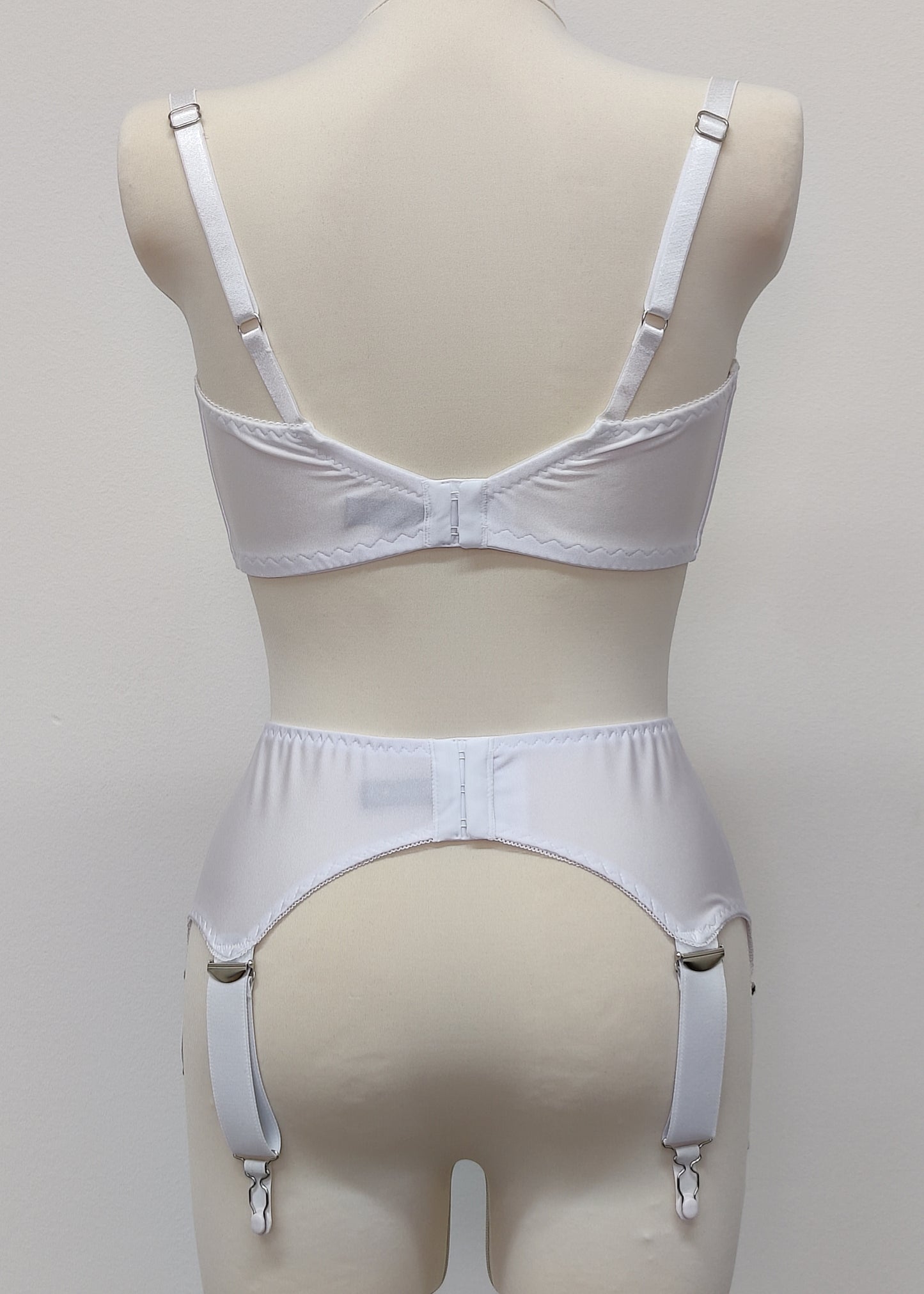 White wide Iris garter belt with a deep V-style design, featuring six extra wide adjustable straps, shown with matching white bra, back view