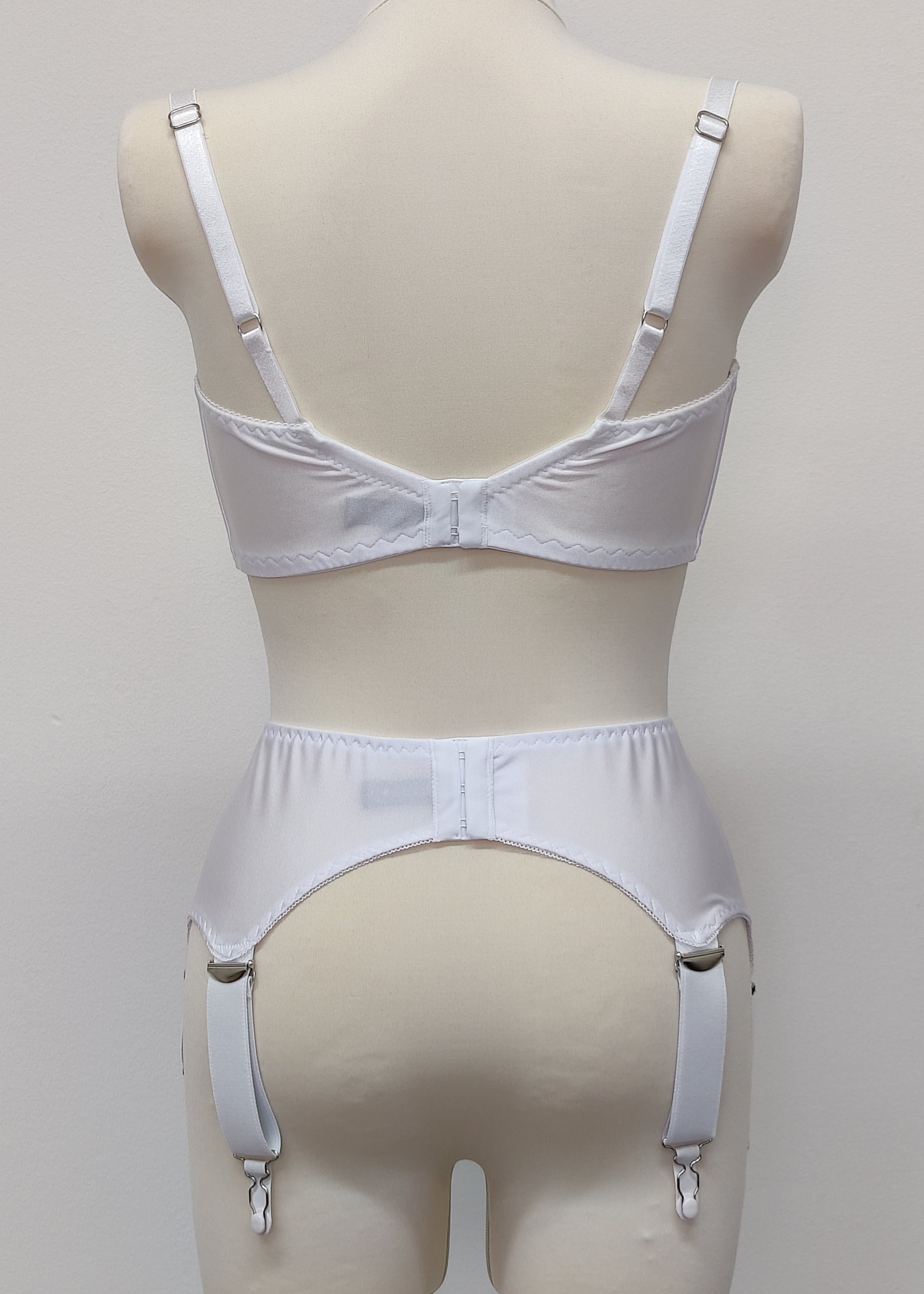 White wide Iris garter belt with a deep V-style design, featuring six extra wide adjustable straps, shown with matching white bra, back view