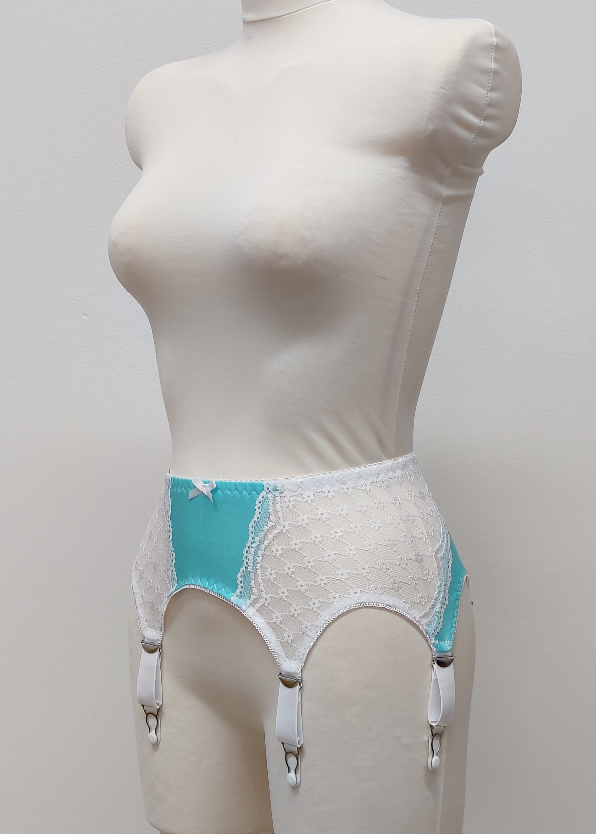 A white lace and Aqua blue Lycra, Mona garter belt with 6 adjustable straps and hook and eye closure, displayed on a mannequin, side view