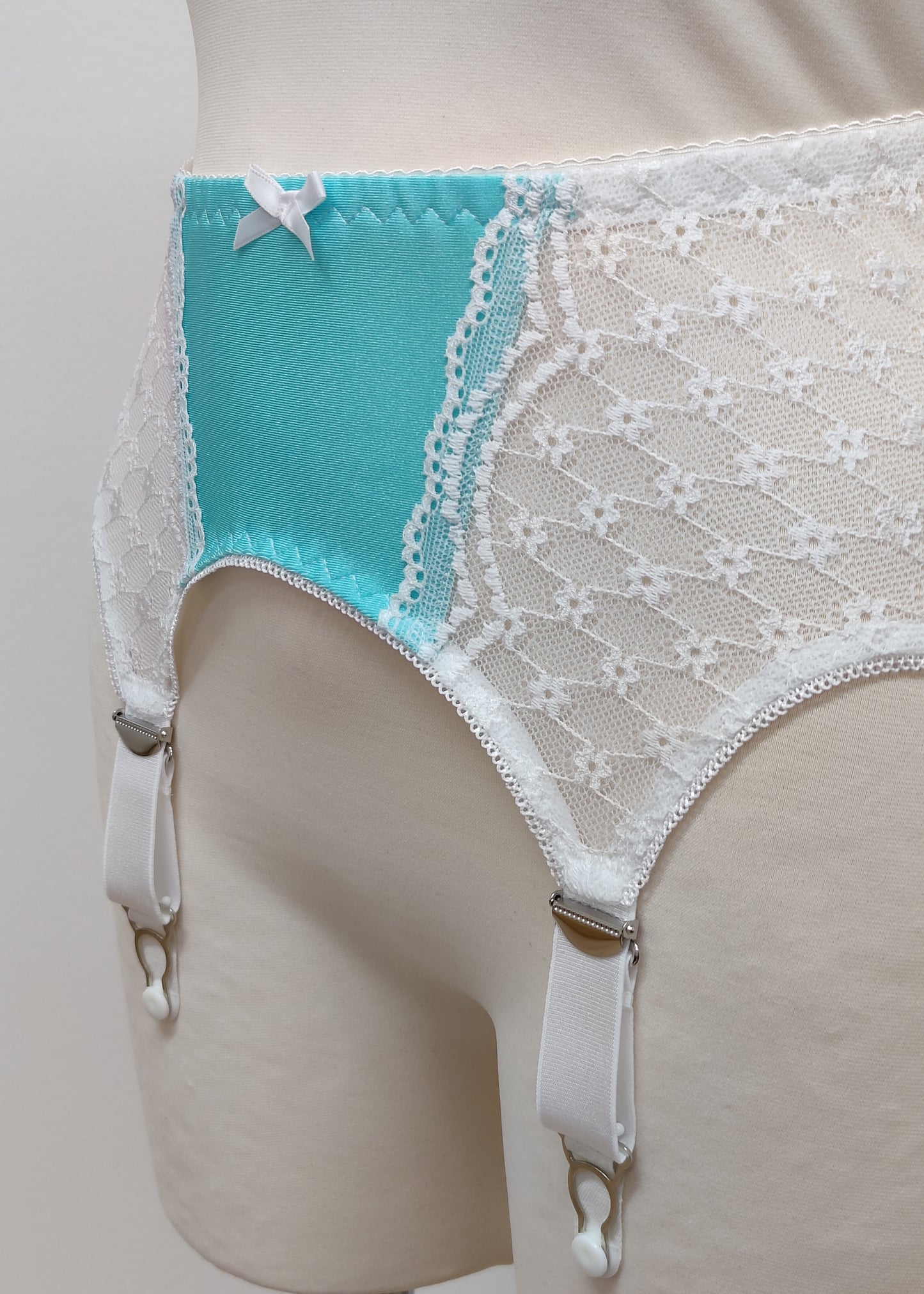 A white lace and Aqua blue Lycra, Mona garter belt with 6 adjustable straps and hook and eye closure, displayed on a mannequin. Detail