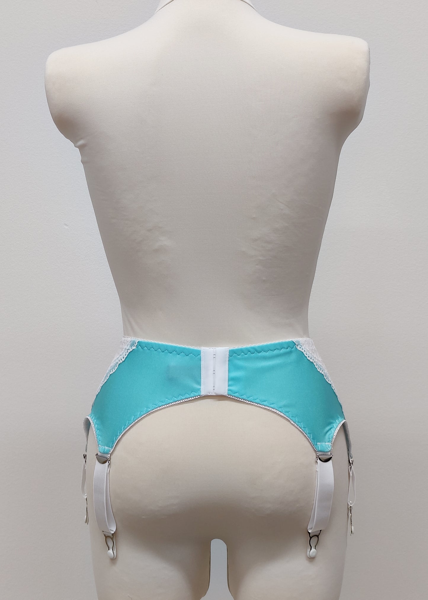A white lace and Aqua blue Lycra, Mona garter belt with 6 adjustable straps and hook and eye closure, displayed on a mannequin. Back view