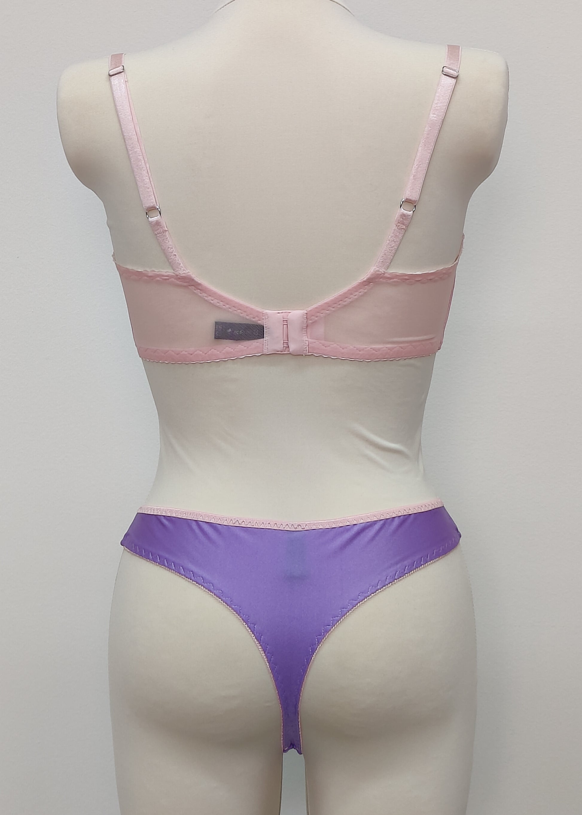 Mannequin wearing a pink Lucy bra and purple Mia thong underwear with pink sheer side panels , back view