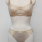Beige lingerie set on a mannequin against a plain background. Zigi thong with side lace panels and Alice bra