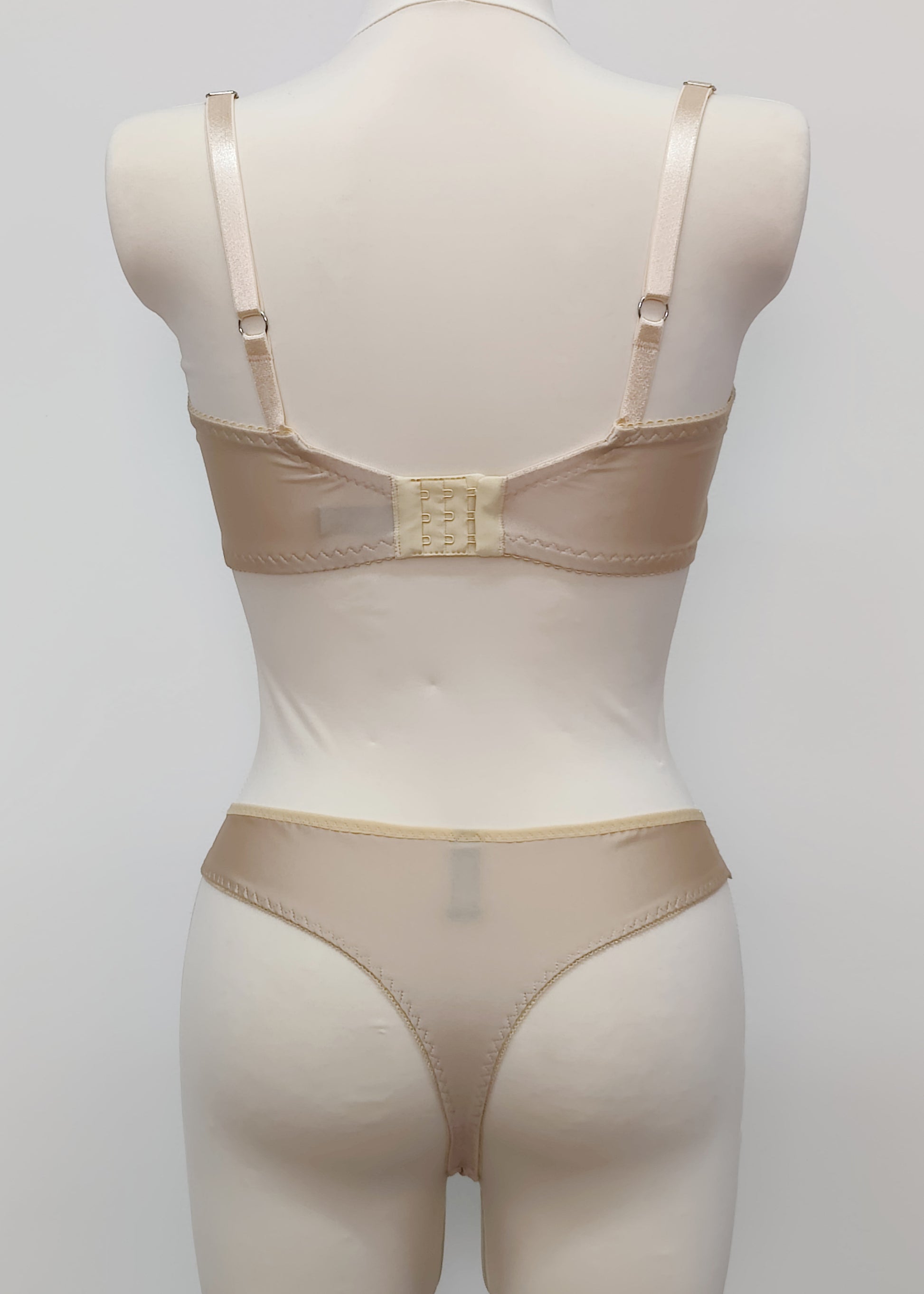 Beige lingerie set on a mannequin against a plain background. Zigi thong with side lace panels and Alice bra, back view
