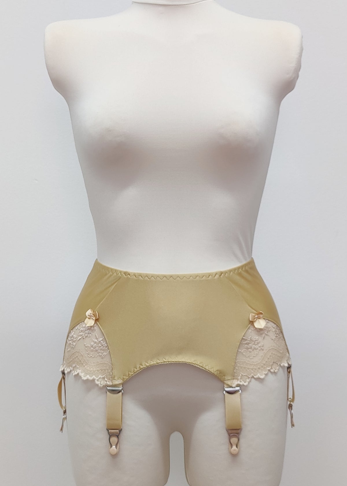 Beige high-waisted garter belt with lace side panels and hanging suspenders, displayed on a white mannequin torso against a light gray background.