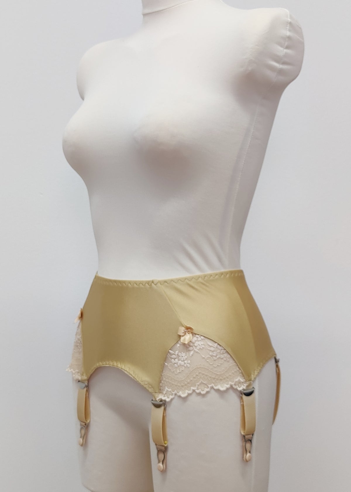 Beige high-waisted garter belt with lace side panels and hanging suspenders, displayed on a white mannequin torso against a light gray background.