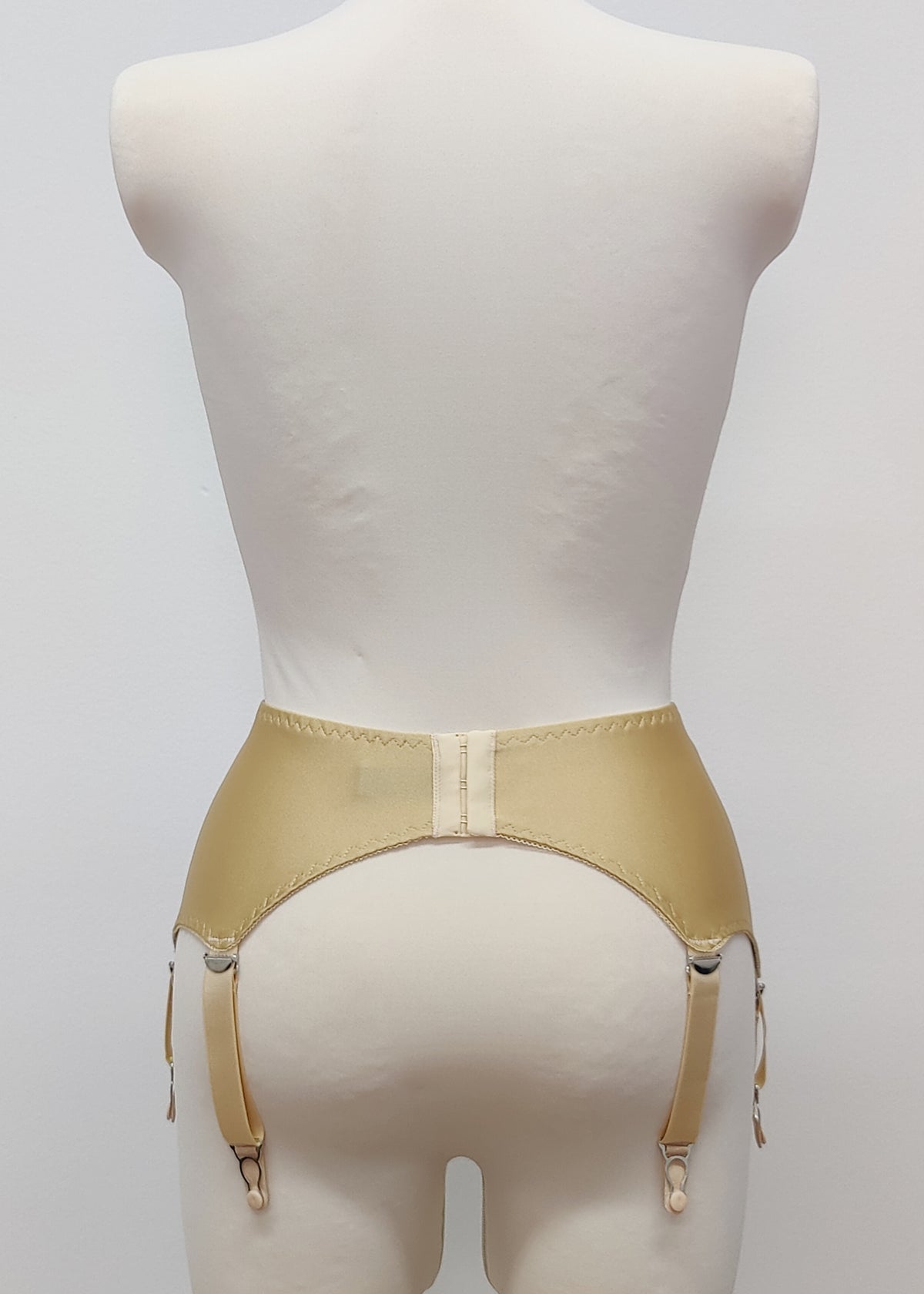 Beige high-waisted garter belt with lace side panels and hanging suspenders, displayed on a white mannequin torso against a light gray background.
