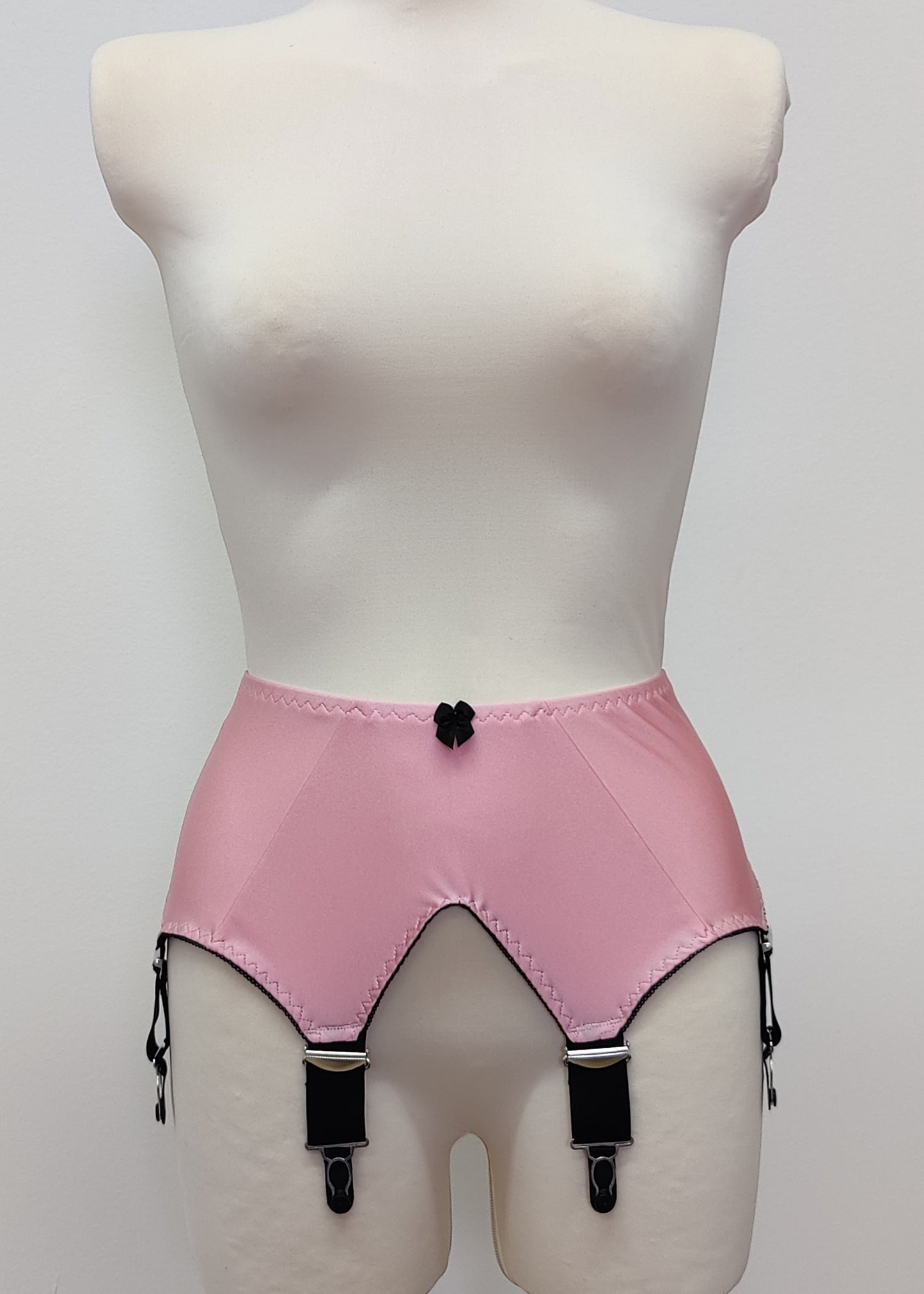 Pink high-waisted garter belt with black trim and black clips, displayed on a white mannequin torso against a light gray background.