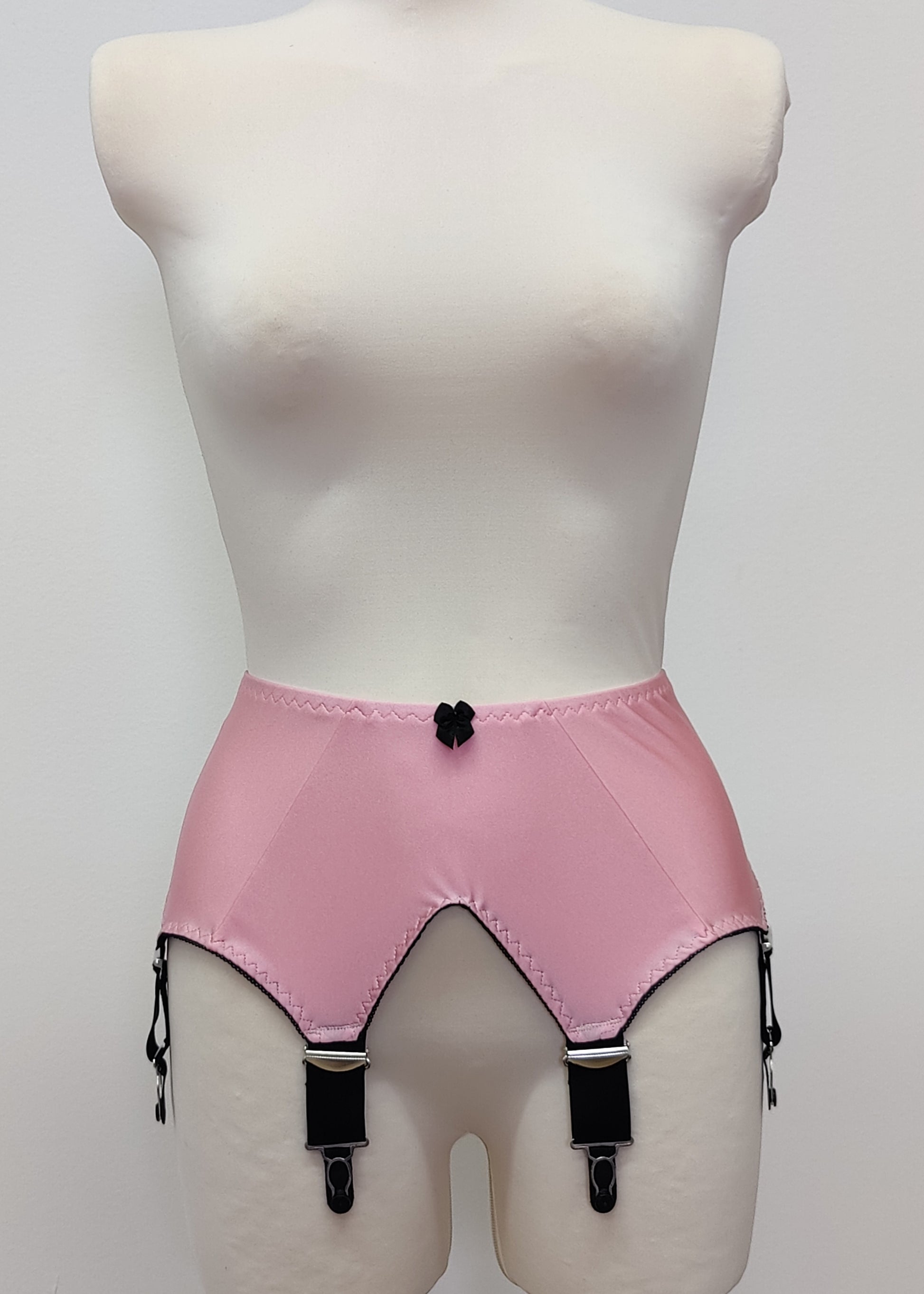 Pink high-waisted garter belt with black trim and black clips, displayed on a white mannequin torso against a light gray background.